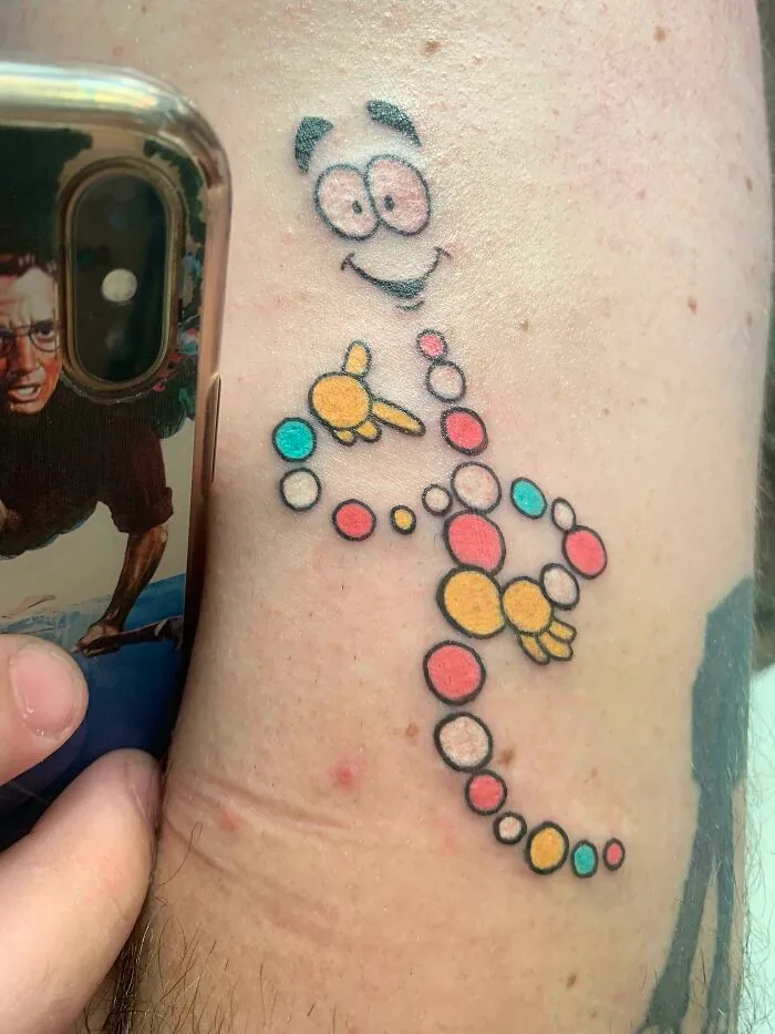 Colorful psychedelic tattoo featuring abstract shapes and a smiling face on an arm.