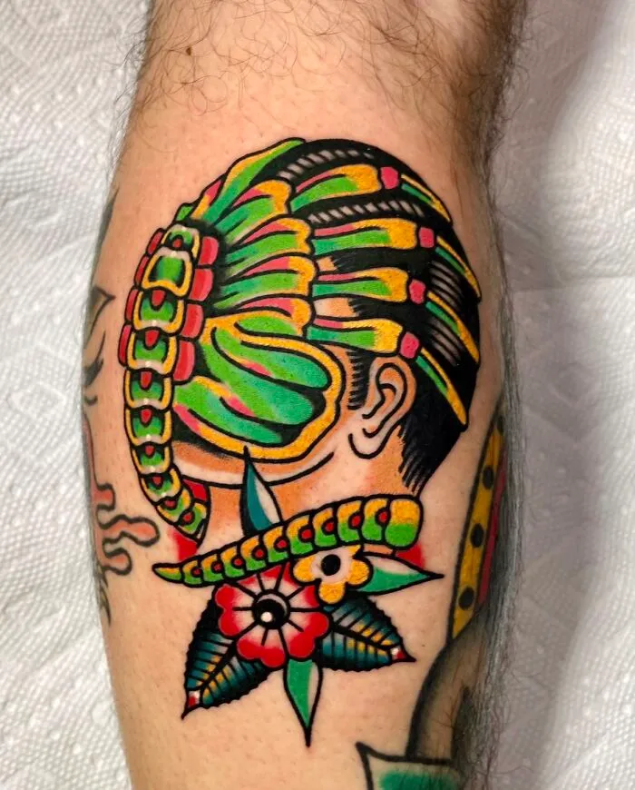 Colorful trippy tattoo of a facehugger on a leg, featuring vibrant greens and reds with floral elements.