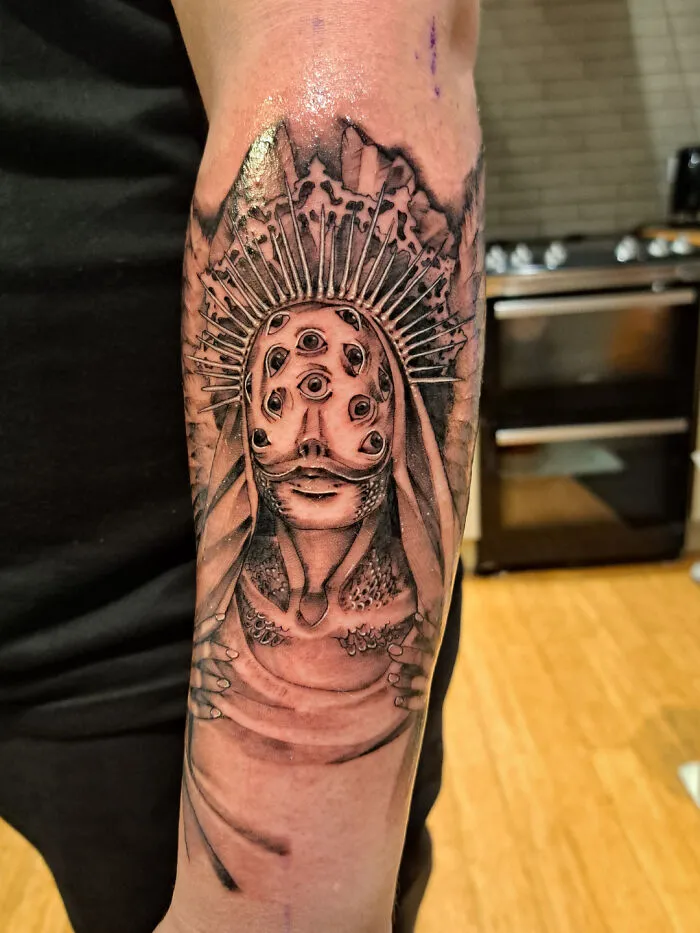 Trippy arm tattoo featuring a multi-eyed monster design in black ink.