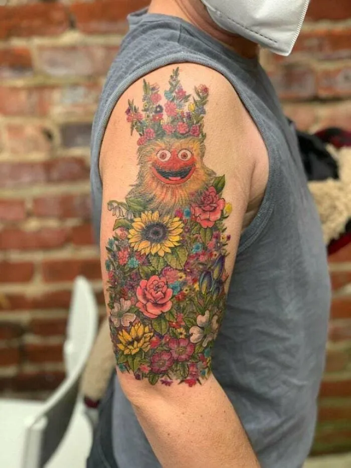 Trippy flower monster tattoo on shoulder with vibrant colors and detailed floral design.