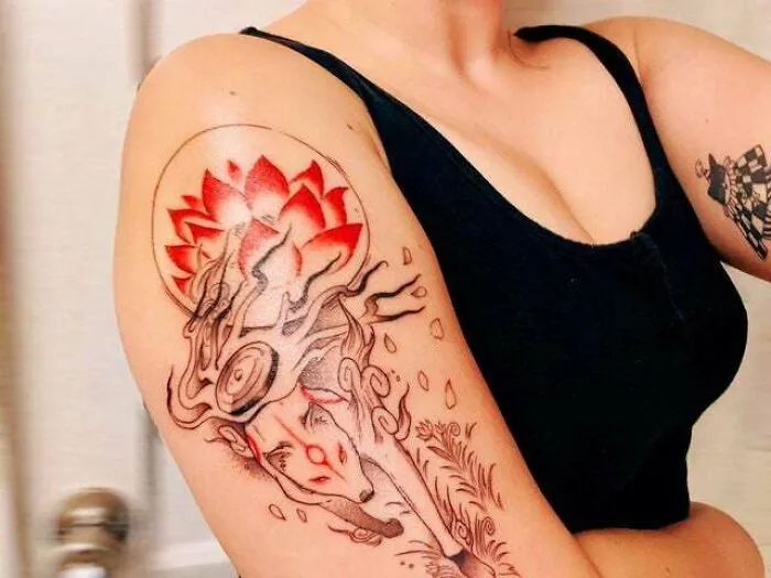 Colorful psychedelic art tattoo featuring a surreal face and lotus design on a person's upper arm.