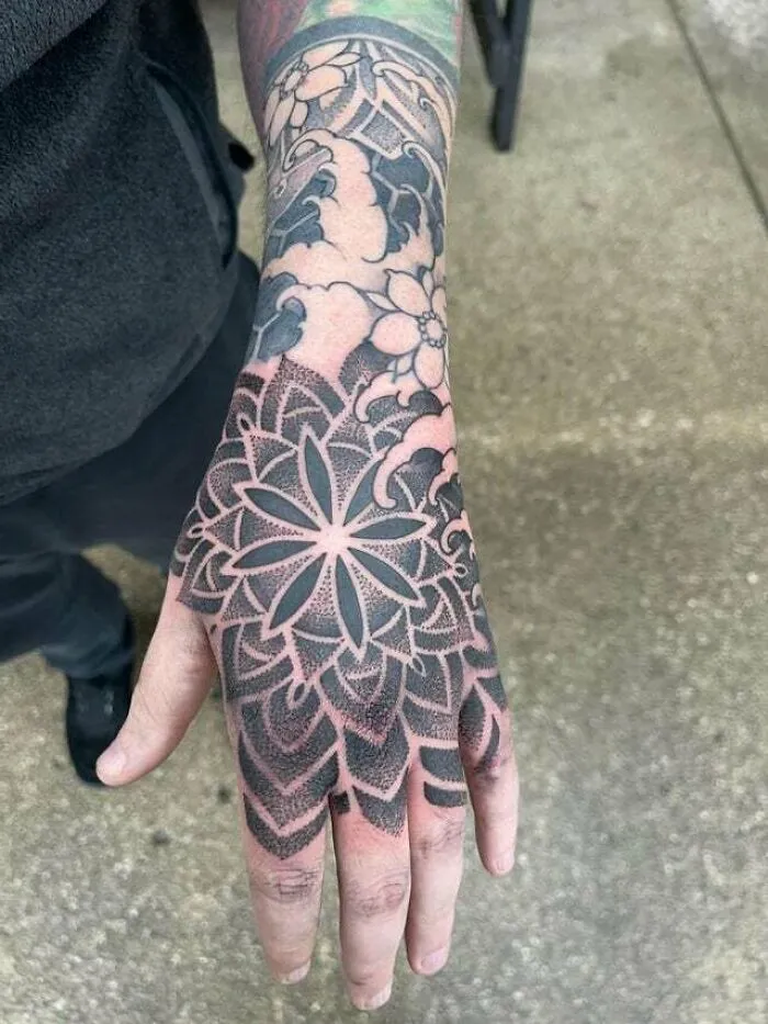 Hand with an intricate, psychedelic art-inspired tattoo featuring floral and geometric patterns.