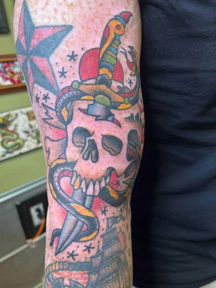 Tattoo of a skull with a colorful snake and dagger, featuring trippy designs and symbols on an arm.