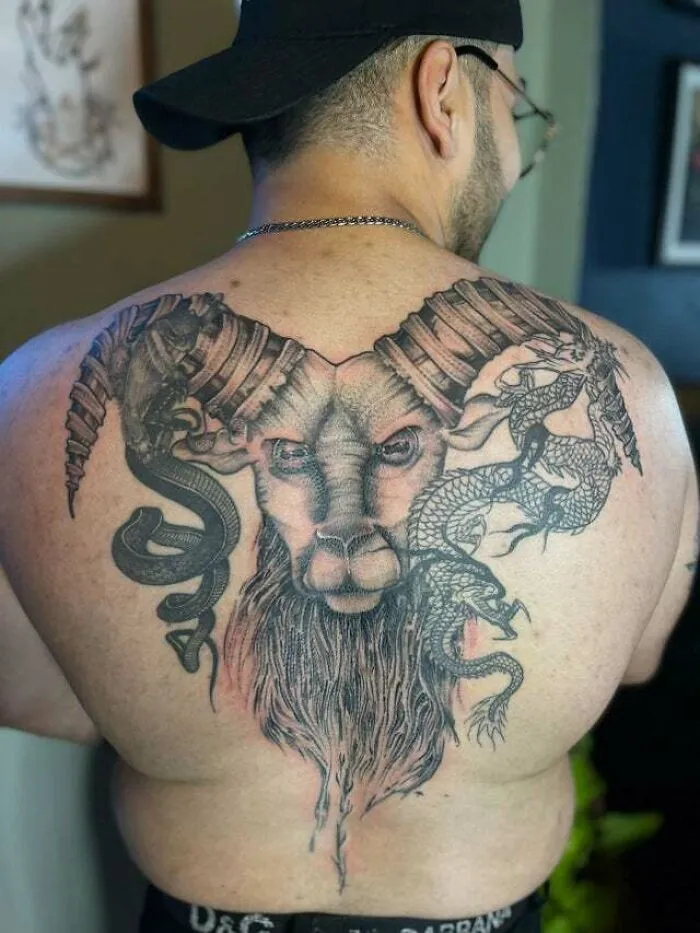 Man with trippy Capricorn sea-goat tattoo on his back, featuring detailed horns and mythical elements.