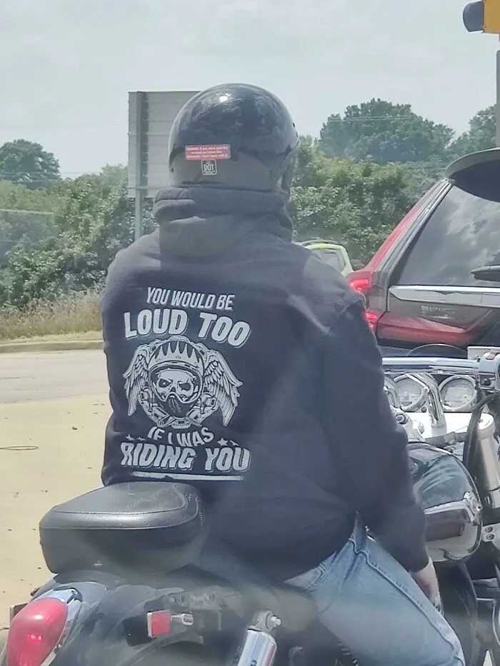 Rider wearing a helmet and hoodie with humorous text, capturing a cringe-worthy moment on a motorcycle.