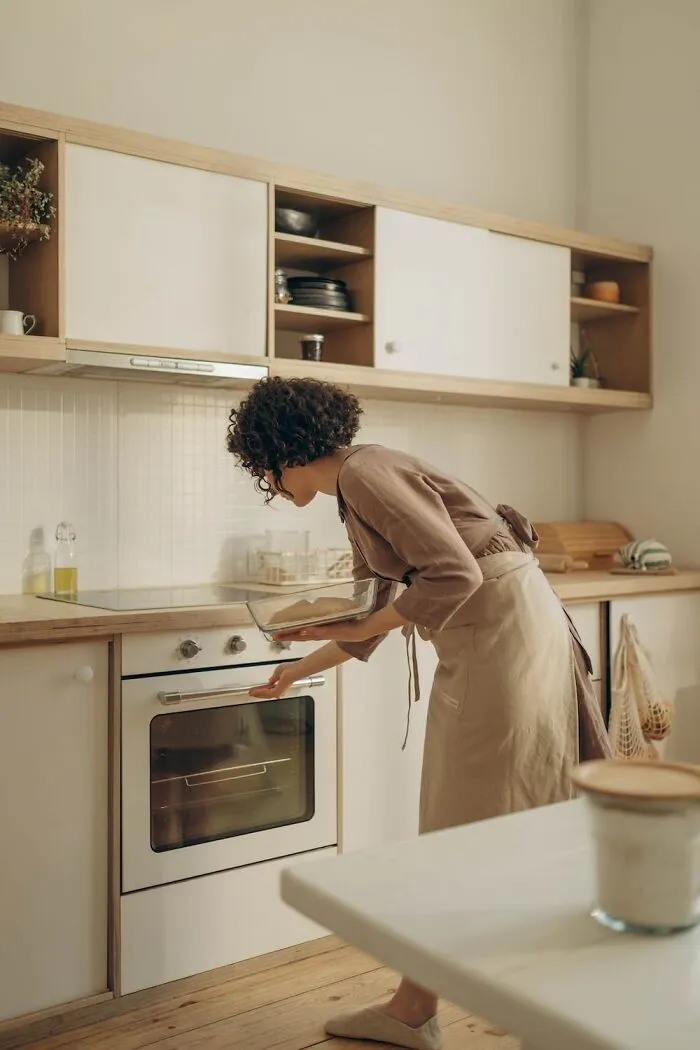 Person baking in a cozy kitchen for New Year’s Eve, wearing an apron and using a modern oven, creating a festive meal.