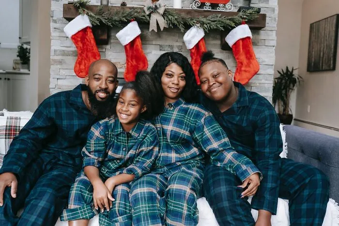 Family in matching pajamas smiling by a fireplace with stockings, celebrating New Year’s Eve together.