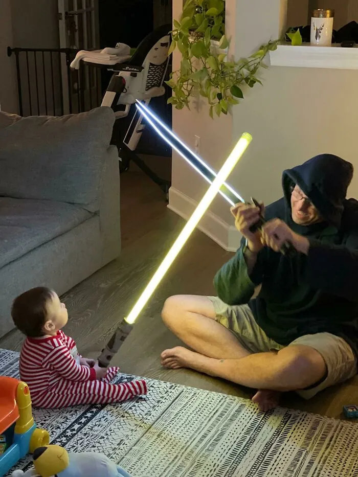 Man and baby wielding toy lightsabers in a humorous Christmas scene.