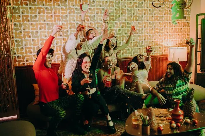 People celebrating New Year's Eve indoors, wearing festive outfits, raising glasses in a cheerful atmosphere.
