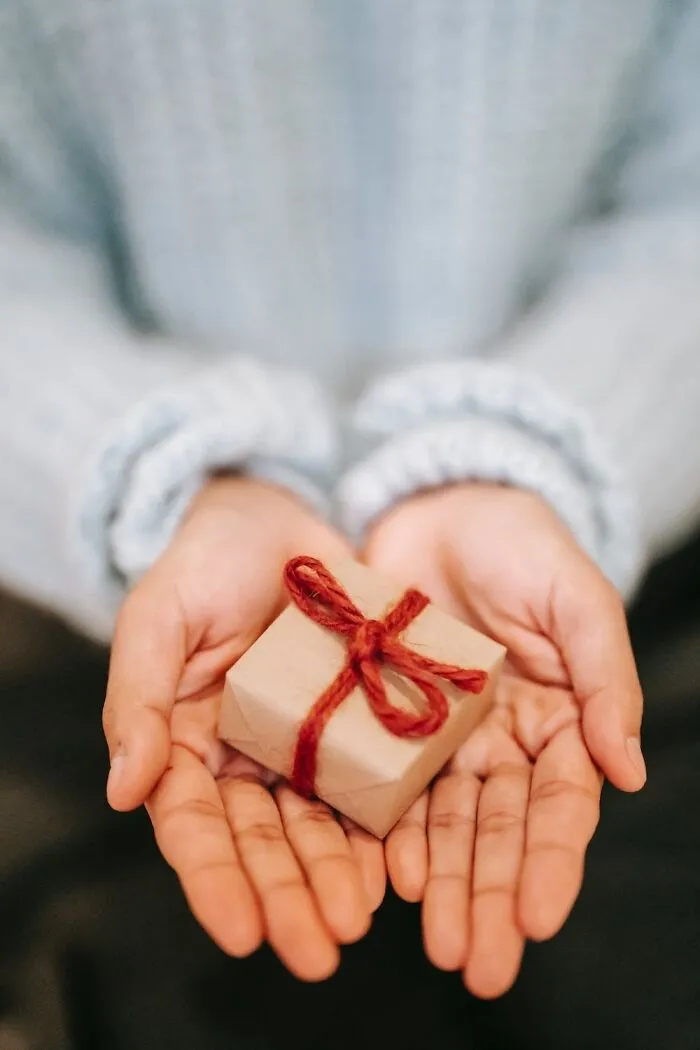 Hands holding a small gift wrapped with red twine, perfect for New Year’s Eve celebrations.