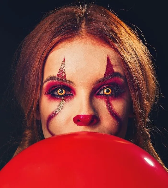 Woman in clown makeup holding a red balloon, perfect for cool New Year's Eve festivities.