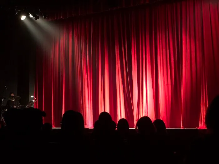 Red theater curtains on stage with audience silhouettes, illuminated by spotlight for cool New Year’s Eve performance.