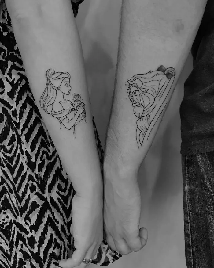 Cartoon tattoos of a woman and a lion on forearms, inspired by animated shows, showcasing artistic line work.