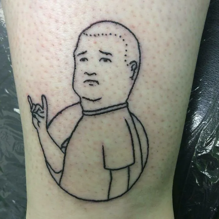 Cartoon-inspired tattoo of a character making a gesture, outlined in black ink on skin.