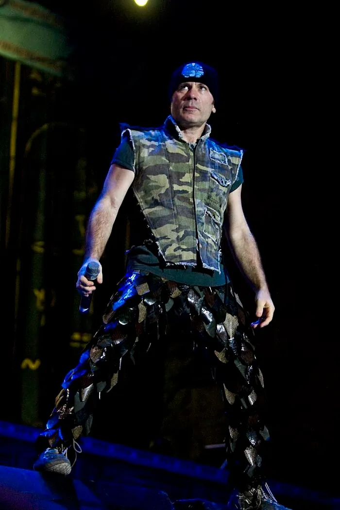 Male celebrity wearing a camouflage vest and unique patterned pants performing on stage, showcasing the smartest celebrities.