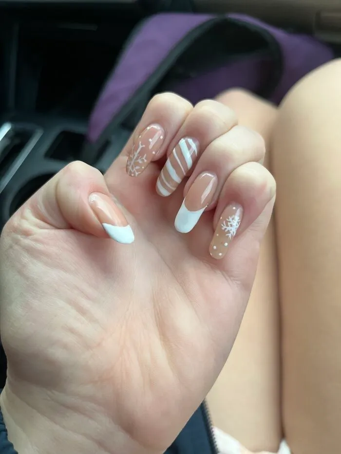 An elegant nude and white French manicure with delicate white snowflakes and stripes for a winter nail art style