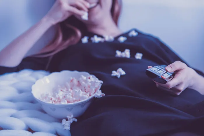Person relaxing with popcorn and remote, enjoying cool New Year’s Eve activities.