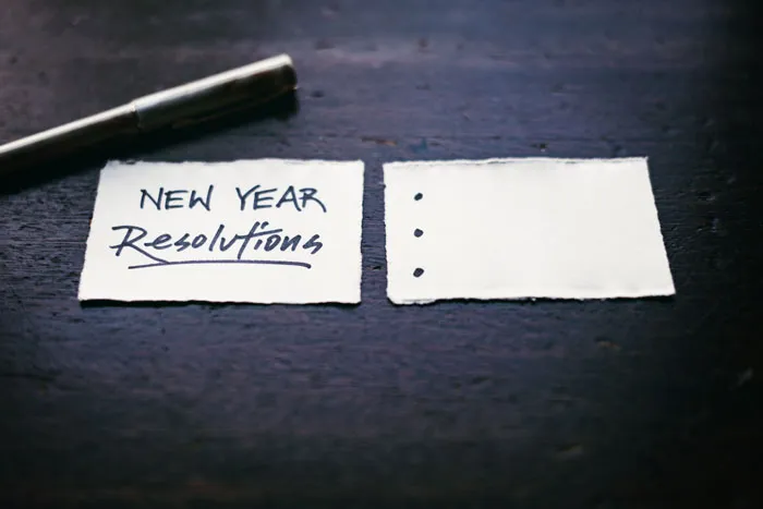New Year's resolutions written on paper with pen on a dark wooden table.