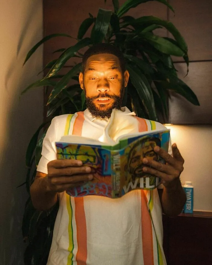 Man reading a colorful book indoors with plant in background, representing smartest celebrities and intelligence.