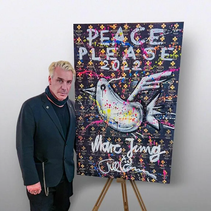 Man standing next to colorful peace-themed artwork, representing talented and intelligent celebrities in creative fields.
