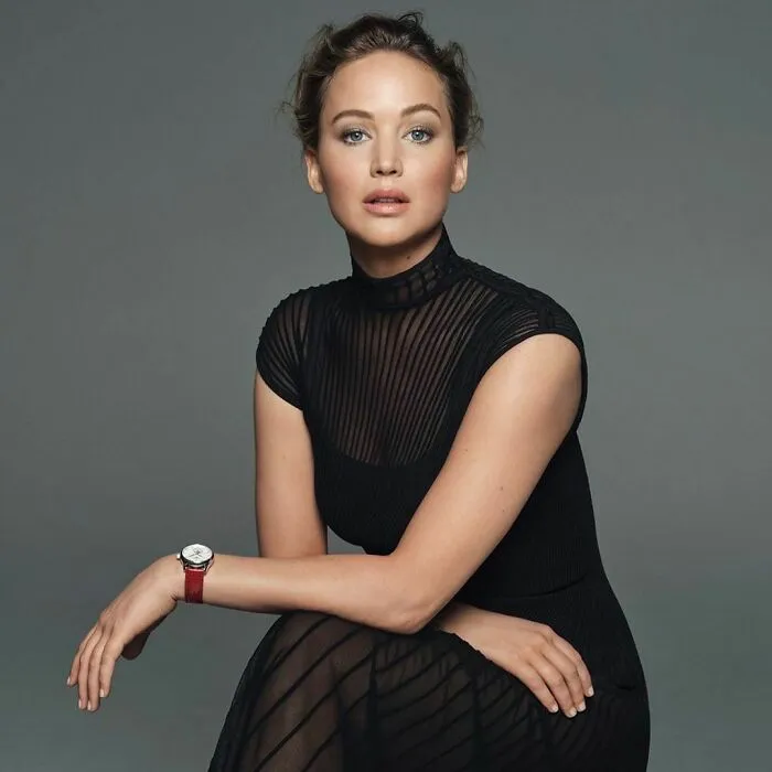Celebrity wearing a black sheer dress and red watch, posing confidently as one of the smartest celebrities known for talent and intelligence