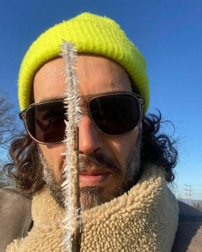 Close-up of a celebrity wearing sunglasses and a yellow beanie holding a frosty stick, showcasing smartest celebrities intelligence.
