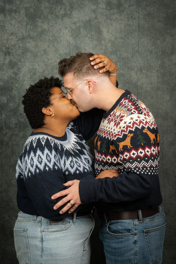 Couple in 80s-themed photoshoot wearing vintage sweaters, sharing a kiss for their anniversary celebration.
