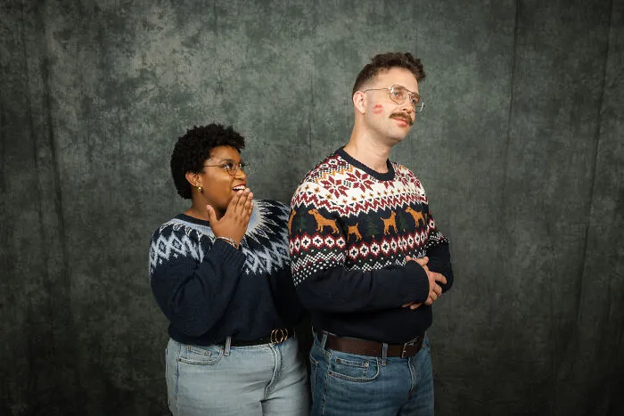 Couple in awkward 80s photoshoot with festive sweaters; husband has lipstick mark on his cheek.
