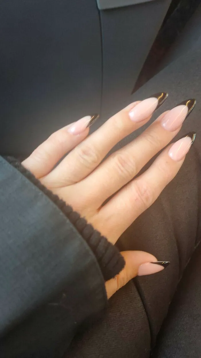 An elegant hand with glossy almond-shaped nails featuring black tips, suitable for winter nail art designs.