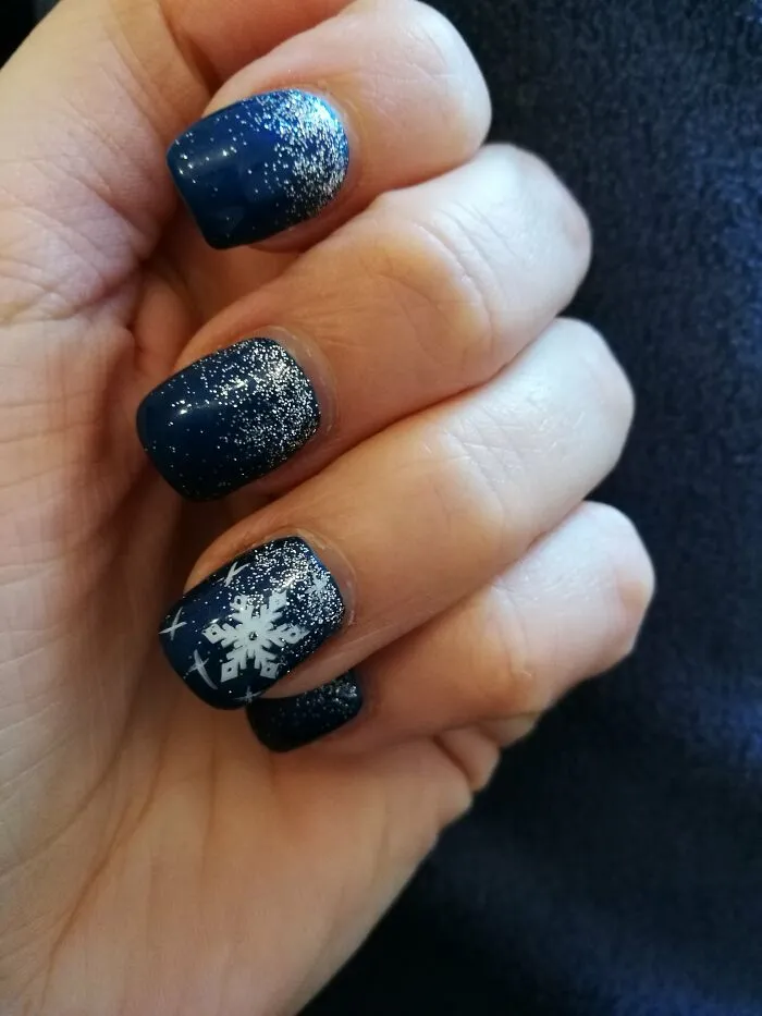 Winter nail art design with dark blue polish, shimmering silver glitter, and a white snowflake accent