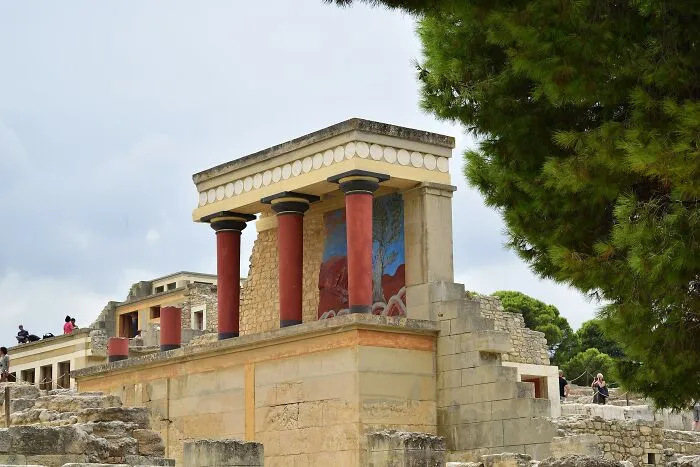 Ancient ruins with red columns at the Knossos Palace, notable artifacts revealing historical information.