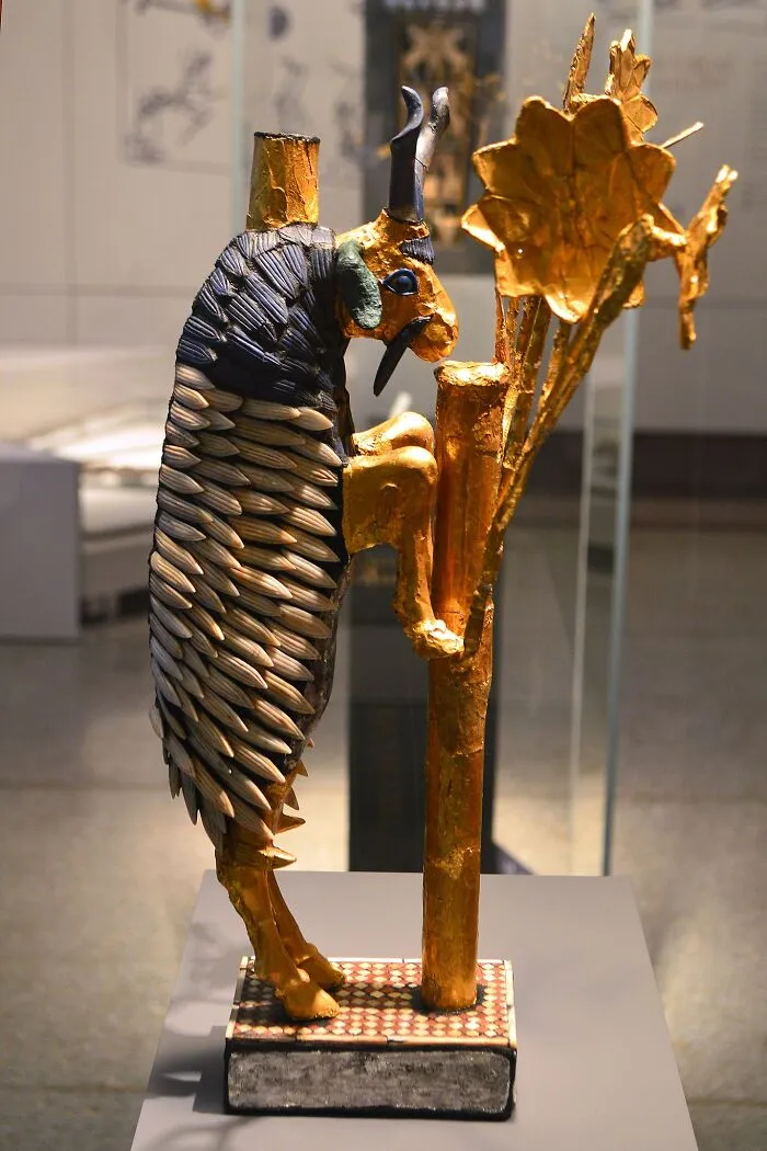 Ancient artifact of a goat standing against a gold-topped reed, showcasing historical significance and intricate craftsmanship.