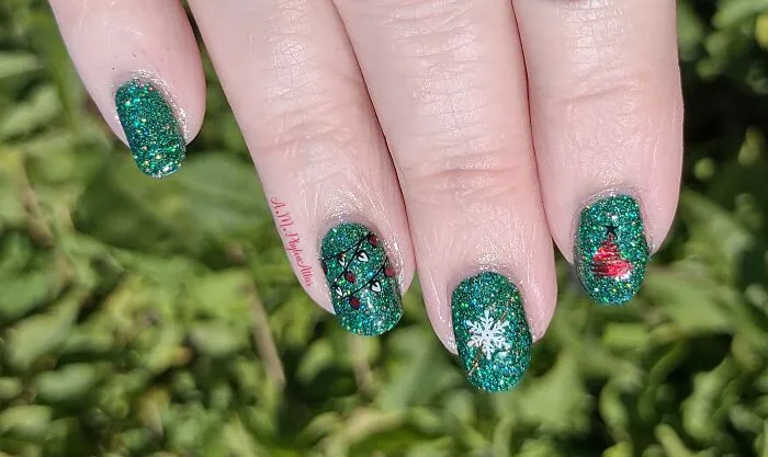 Christmas nail art with a green glitter base featuring a snowflake, string lights, and a tiny red tree