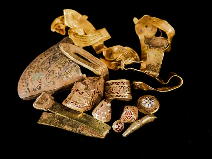 Ancient artifacts including gold jewelry and engraved pieces on black background.