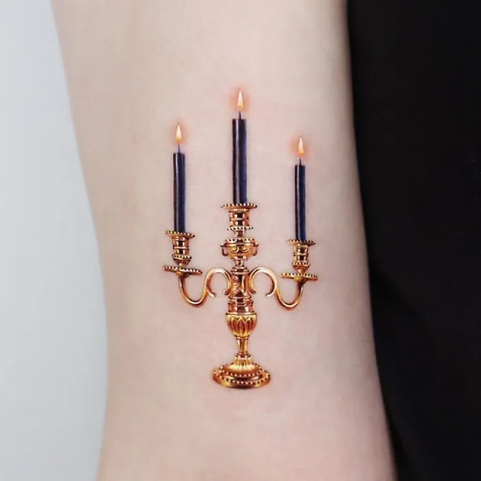 Golden tattoo of a detailed candelabra on skin, created by a Manhattan-based tattoo artist.
