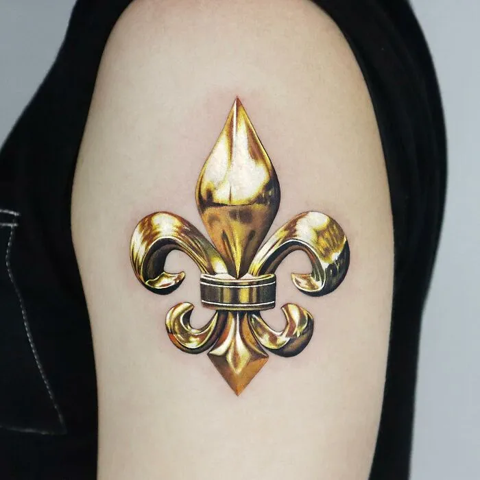 Golden fleur-de-lis tattoo on arm, showcasing precision by Manhattan-based artist.