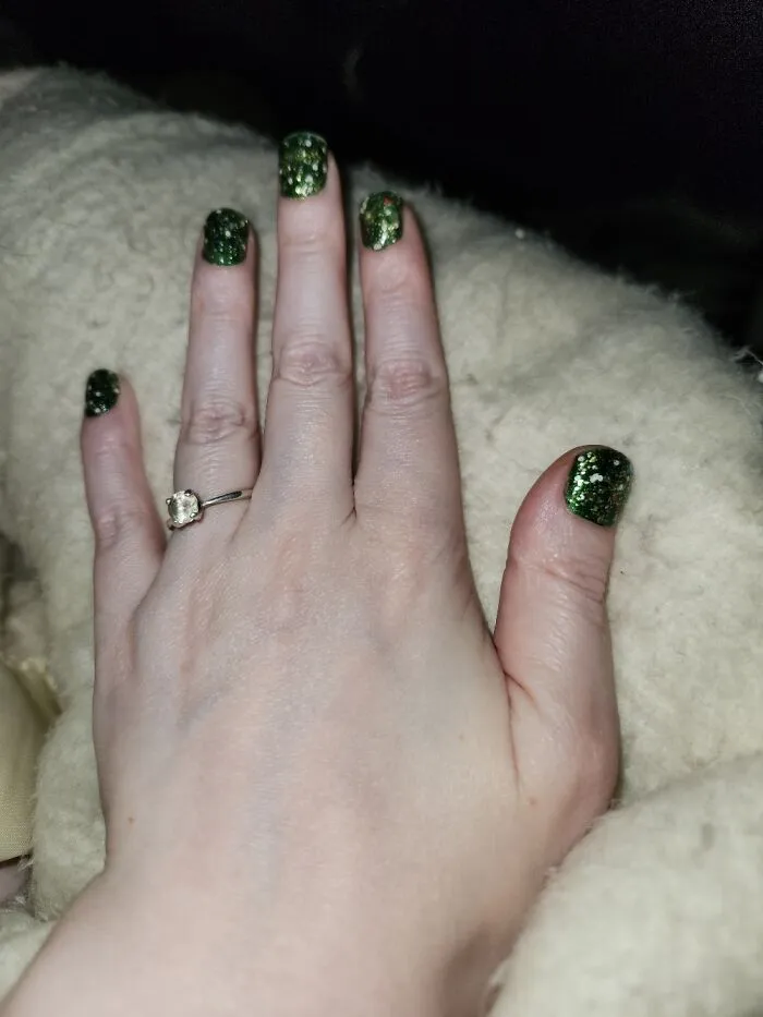 Simple winter nail art featuring deep green polish with sparkling glitter on short nails