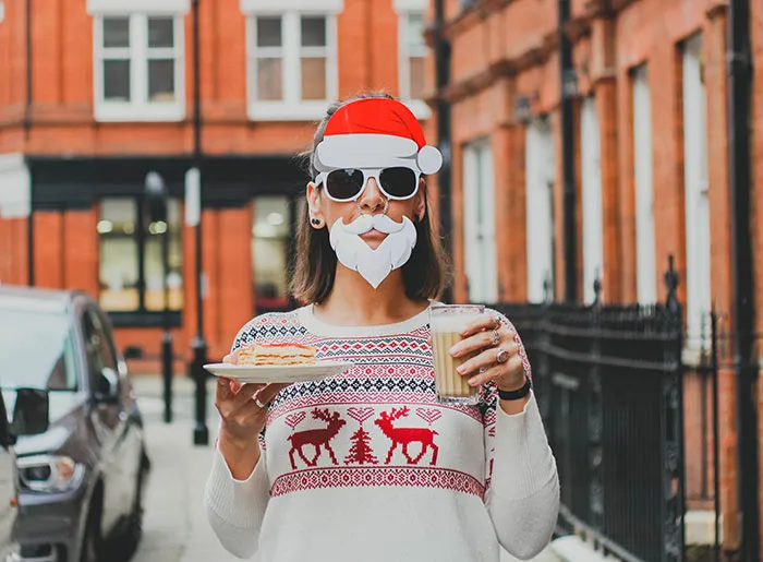 Person wearing Christmas sweater, Santa mask and drink with food