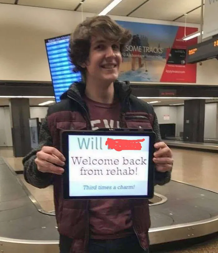 Smiling person at airport with humorous welcome sign, adding humor to Christmas travel.