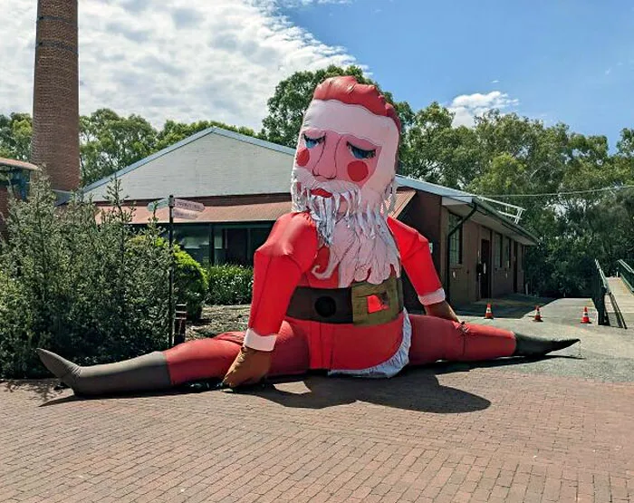 Inflatable Santa doing splits, adding humor to a Christmas scene outside a building.