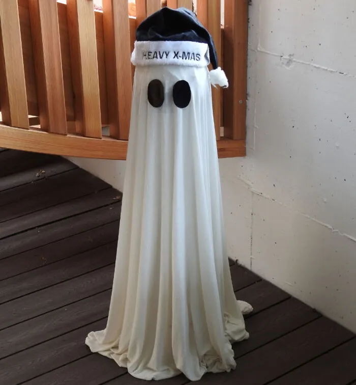 Ghost costume with a Santa hat labeled "Heavy X-Mas" on a wooden deck exemplifies Christmas humor.