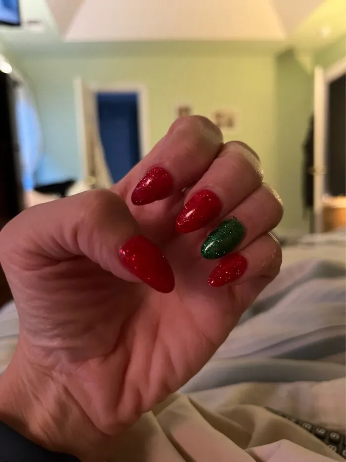 A hand showing red and green glittery Christmas nail art designs.