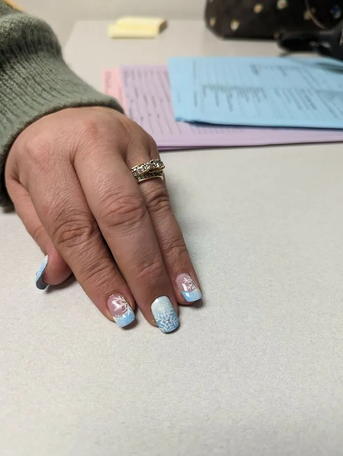 Winter nail art with light blue tips and white snowflake designs on a hand with a gold ring