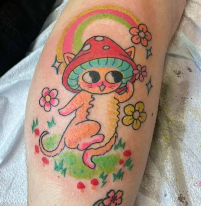 Trippy tattoo of a cat with a mushroom hat and flowers on an arm.