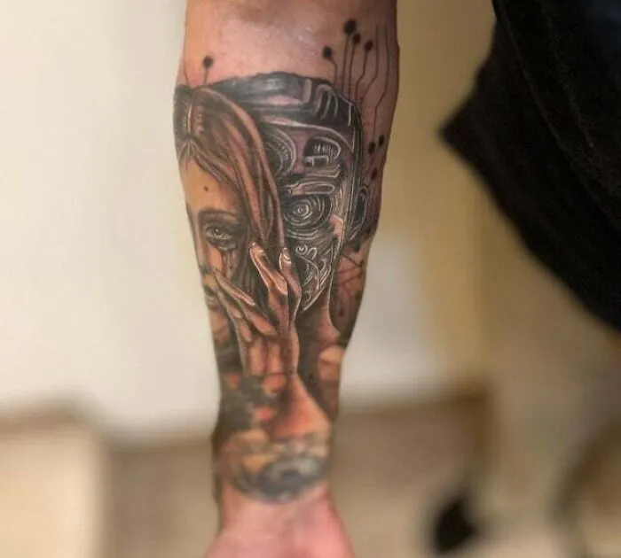 A forearm tattoo featuring a trippy fusion of a woman's face and a robotic arm design.
