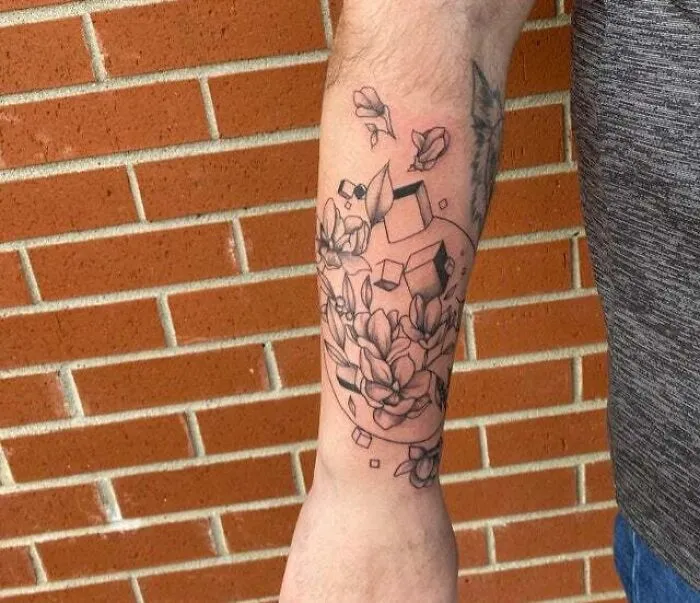 Trippy tattoo of flowers and cubes on arm, blending geometric and organic designs.