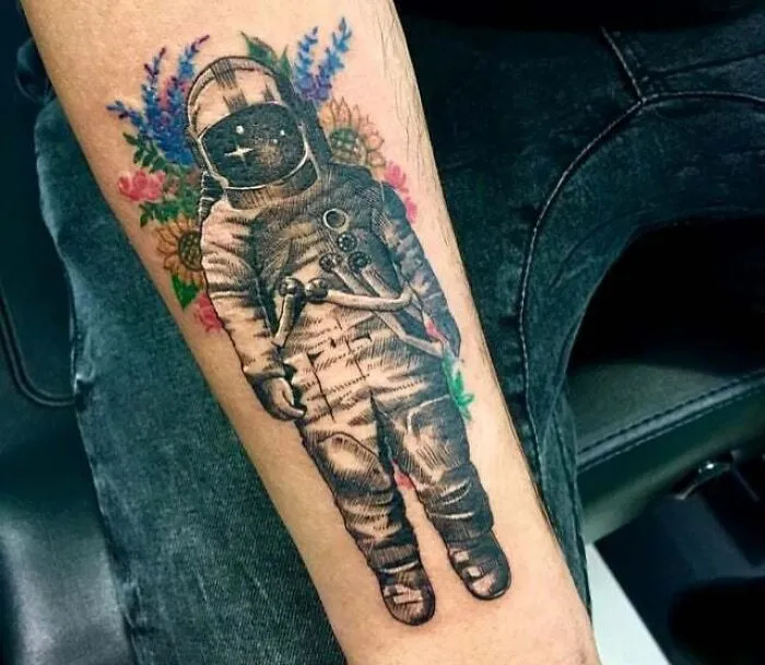 Astronaut with floral design tattoo on arm, showcasing a trippy tattoo idea.
