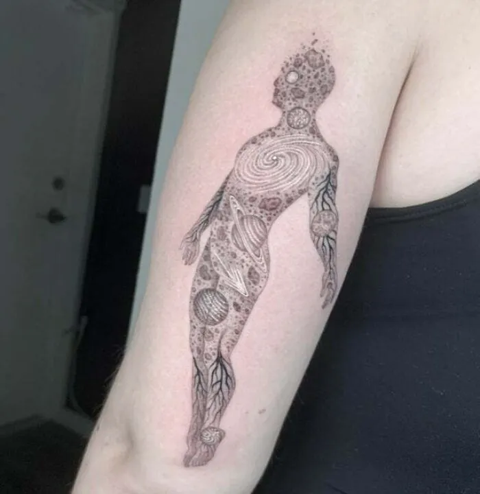 Trippy tattoo of a space universe figure on a man's arm, featuring planets and cosmic designs.