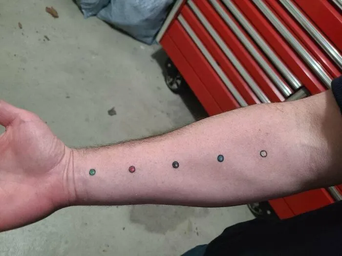 Minimalist tattoo of colorful dots on a forearm, set against a workshop background with a red toolbox.