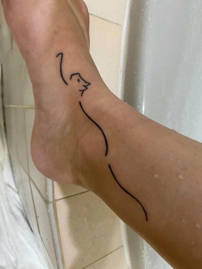 Minimalist tattoo of a cat outline on an ankle, showcasing simple and aesthetically pleasing design.